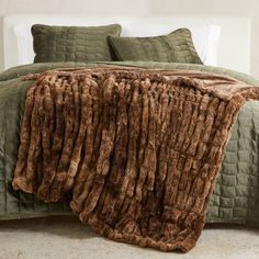 a bed covered in brown fur with pillows and blankets on top of the bedspread