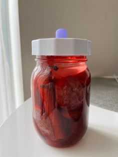 a jar filled with pickles sitting on top of a white table next to a window