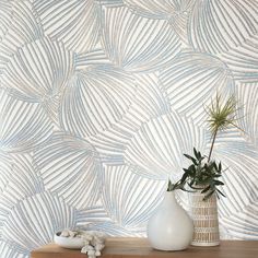 a white vase sitting on top of a wooden table next to a wallpapered background