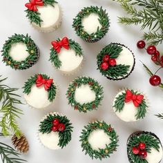 twelve cupcakes decorated with holly and red bows on white frosting, surrounded by greenery