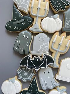 halloween cookies decorated with frosting and icing on a gray tablecloth, including bats, tombstones, ghostes, pumpkins and candles