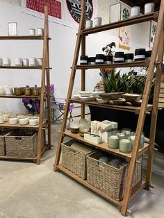 two wooden shelves with baskets and containers on them in a room filled with plants, candles and other items