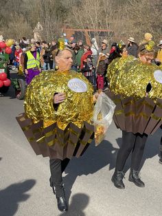 two men dressed in gold and black marching down the street while people watch from behind them