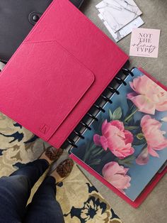 a pink notebook sitting on top of a table next to a person's feet