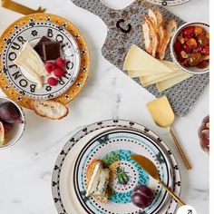 two plates with cheese, fruit and crackers on them sitting on a marble table