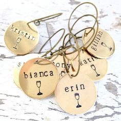 four wine charms with words on them sitting on a table next to each other, one has a glass of wine in it