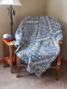 a blue and white blanket sitting on top of a wooden chair next to a lamp