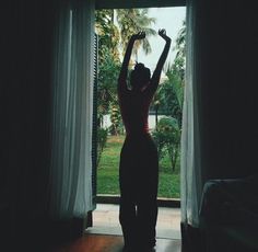 a woman standing in front of a window with her arms up