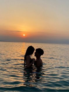 two people in the water at sunset with one holding the other's head and looking into each others eyes