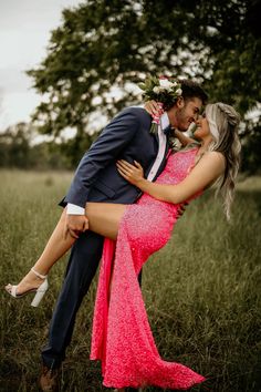 a man in a suit and tie hugging a woman in a pink dress on the grass