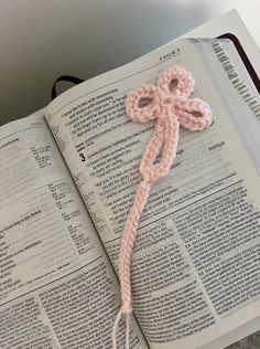 an open book with a pink crocheted knot on top of it, sitting on a table