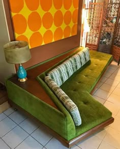 a green couch sitting on top of a white tiled floor next to a lamp and painting