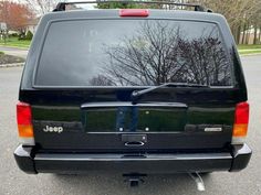 the back end of a black jeep parked in a parking lot next to a tree