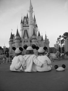 two children sitting on the ground in front of a castle with their heads turned to look like mickey mouses