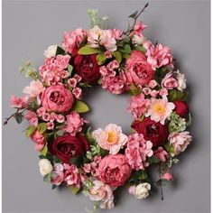 a pink and red flower wreath on a gray background with greenery around it,