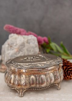 a silver box sitting on top of a table next to a pine cone and flower