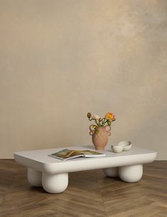 a white table with flowers in a vase on top and magazines sitting on the edge