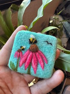 a hand holding a small felted piece with a flower on it's side