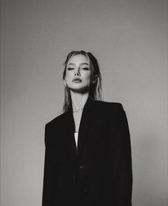 a black and white photo of a woman with long hair wearing a suit, standing in front of a wall