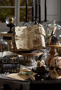 an open book sitting on top of a table next to candles and skulls in glass domes