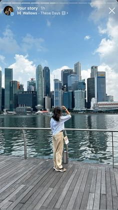 a woman standing on top of a wooden pier next to a body of water with tall buildings in the background