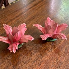 two small pink flowers sitting on top of a wooden table next to eachother