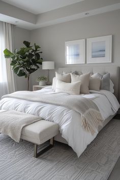 a large bed with white sheets and pillows in a bedroom next to a potted plant