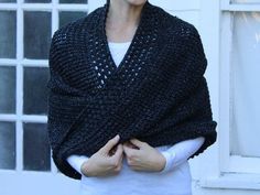 a woman standing in front of a window wearing a black knitted shawl