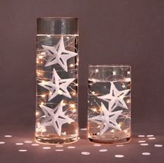 two clear vases filled with water and lit up with white paper stars on them