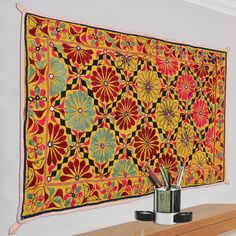 a colorful tapestry hanging on the wall next to a cup with pencils in it