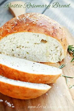 a sliced loaf of bread on top of a wooden cutting board with rosemary sprigs