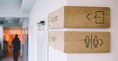 two wooden signs mounted to the side of a white wall next to a hallway with people walking