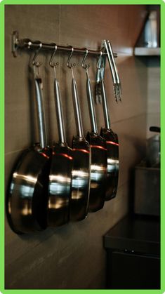 pots and pans are hanging on the wall in this kitchen with stainless steel utensils