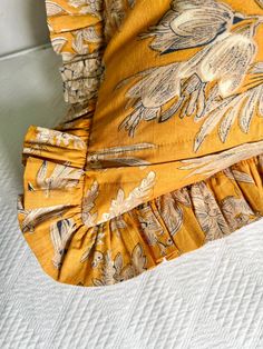 a close up of a yellow dress on a white bed sheet with an orange flowered design