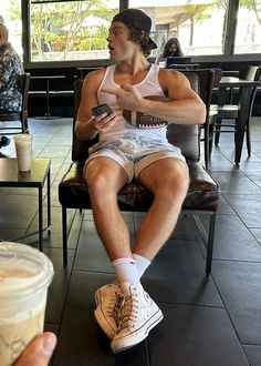 a man sitting in a chair looking at his cell phone while holding a cup of coffee