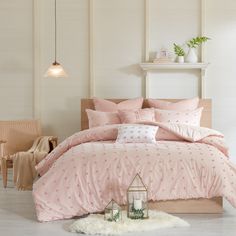 a bed with pink comforter and pillows in a room next to a table, chair and lamp