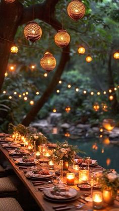 a long table with candles and plates on it in the middle of a forest filled with trees