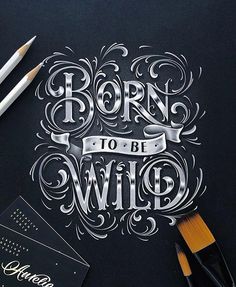 the words born to be wild written on a black paper next to pencils and markers