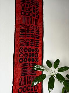 a plant sitting next to a red wall hanging on a white wall with black designs