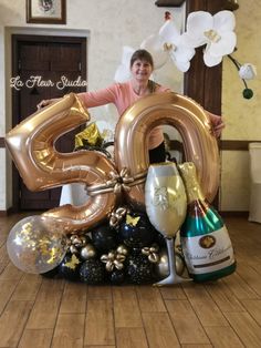 a woman standing next to a large number with balloons and wine bottles on it in a room