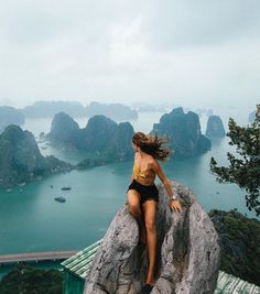 a woman climbing up the side of a cliff with boats in the water behind her