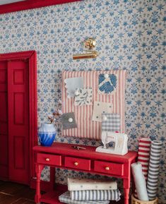 a red desk with blue and white wallpaper next to a red door in a room