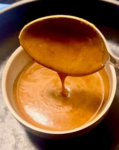 a spoon is pouring sauce into a bowl