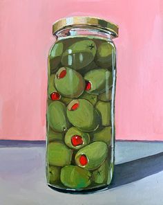 a jar filled with green olives on top of a table next to a pink wall