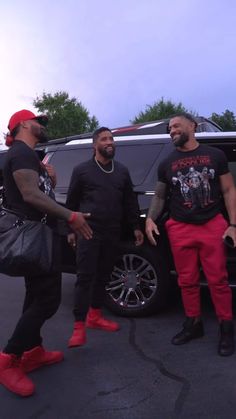 three men standing in front of a car talking to each other and one holding a handbag