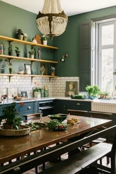 a kitchen with green walls and wooden table surrounded by shelves filled with potted plants