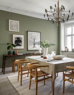 a dining room with green walls and wooden chairs, a chandelier and pictures on the wall