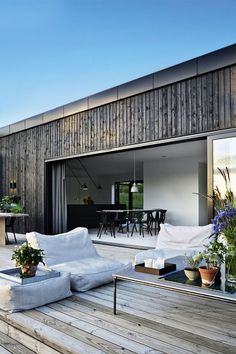 an outdoor living area with white couches and wooden flooring on the outside deck