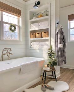 a white bath tub sitting under a window next to a shelf filled with folded towels