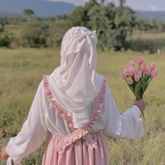 a woman in a pink dress is walking through the grass with flowers on her hand